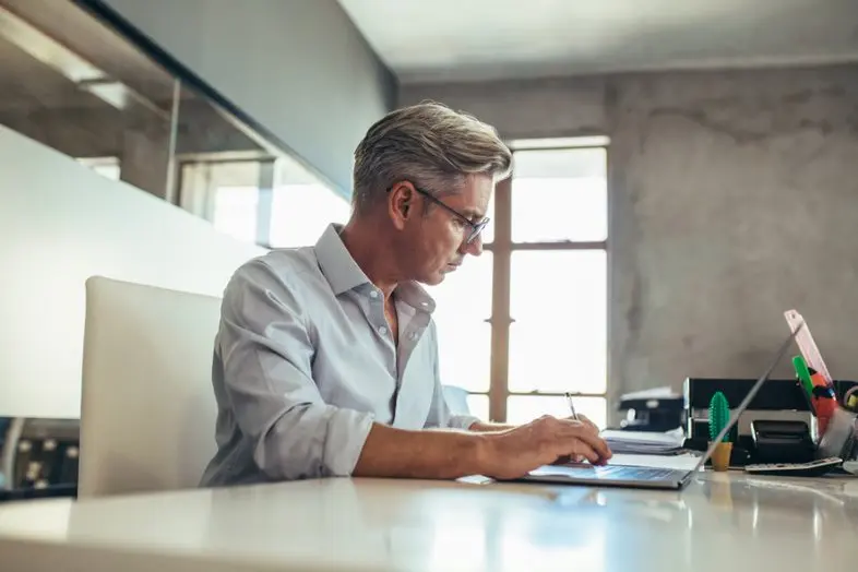 Businessman using laptop reviewing insurance policy.