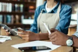 Café workers handling receipts and a tablet