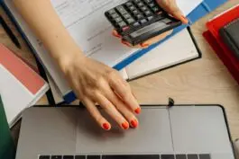 Person using calculator and laptop at desk.