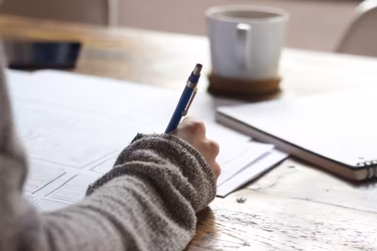Person writing notes at a wooden desk.