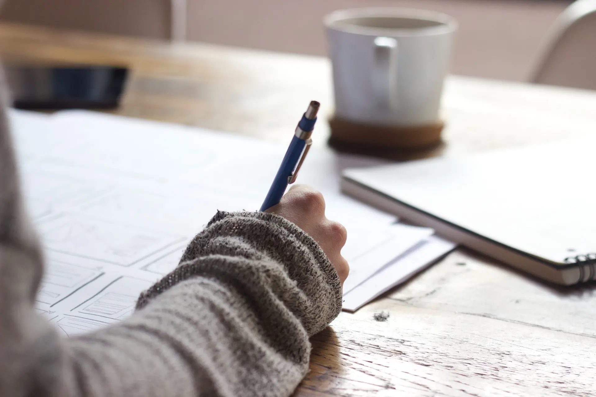 Person writing notes at a wooden desk.