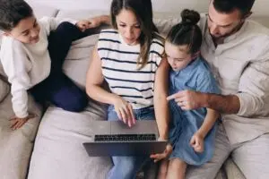 Family browsing laptop together on a couch.