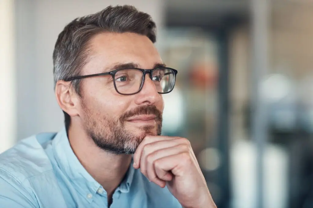 Contemplative man with glasses and beard, indoors.