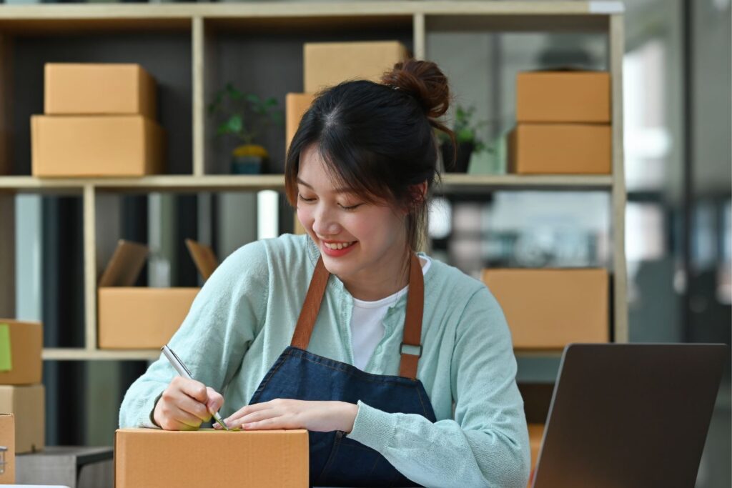 Woman writing on cardboard box, smiling, in store.